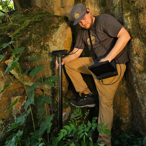 Person with metal detector in a rocky forest setting